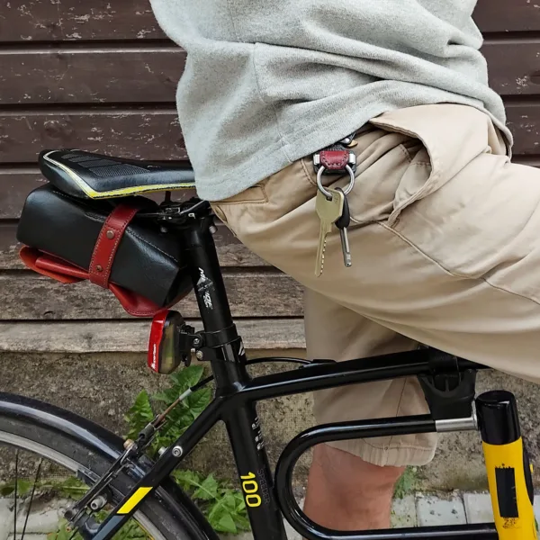 Cycling leather key holder worn on the side of a belt, showing free leg movement in an urban summer setting with saddle bag visible.