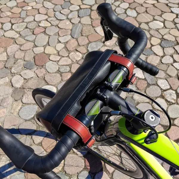 Top view of leather handlebar bag mounted on carbon road bike over cobblestone path