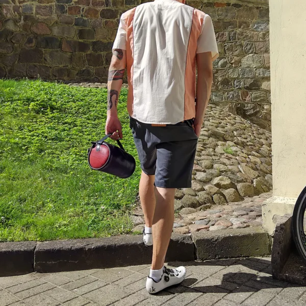 Man walking in cycling shoes, carrying leather handlebar bag
