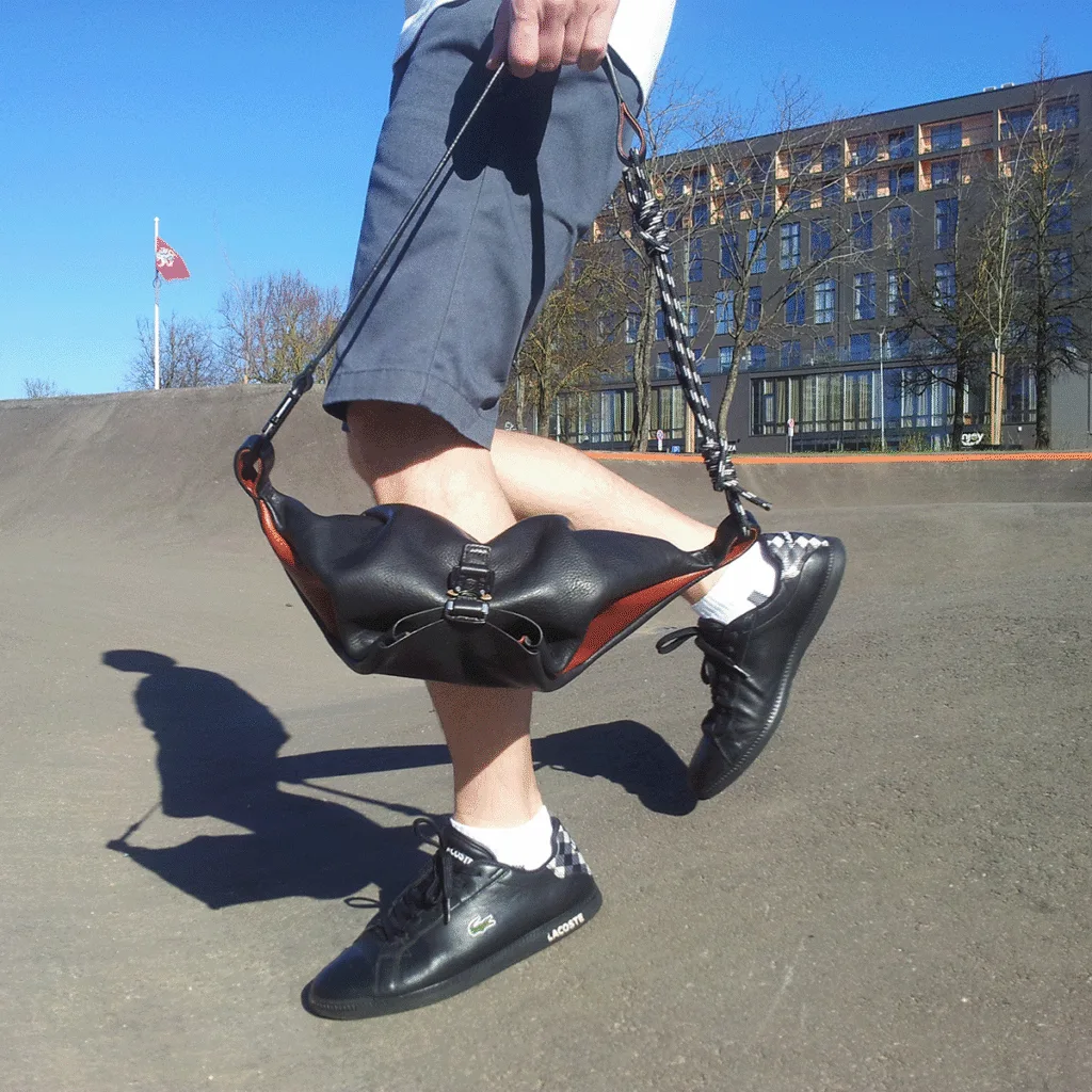 Man holding leather sling bag at urban skate park