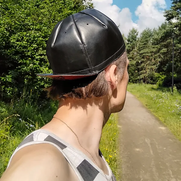 Man wearing a cycling cap styled with relaxed urban outfit, photographed on a park walking trail.